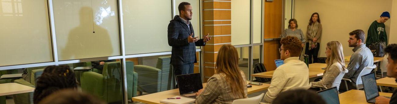 An instructor stands at the front of the class explaining a topic to students.